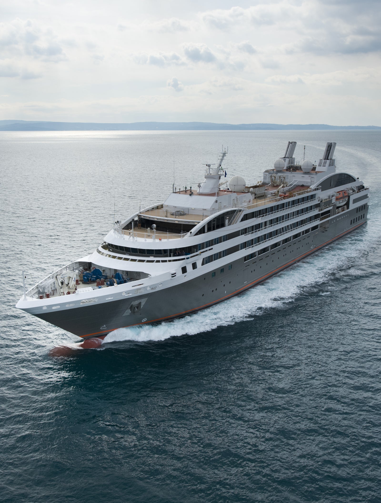 Fincantieri | Group - Business - Products - Cruise Ships - Le Boreal: Sleek modern cruise ship in operation navigating calm open waters under cloudy sky, multiple decks and visible chimneys, setting emphasizes premium travel experience, tranquility and adventure.