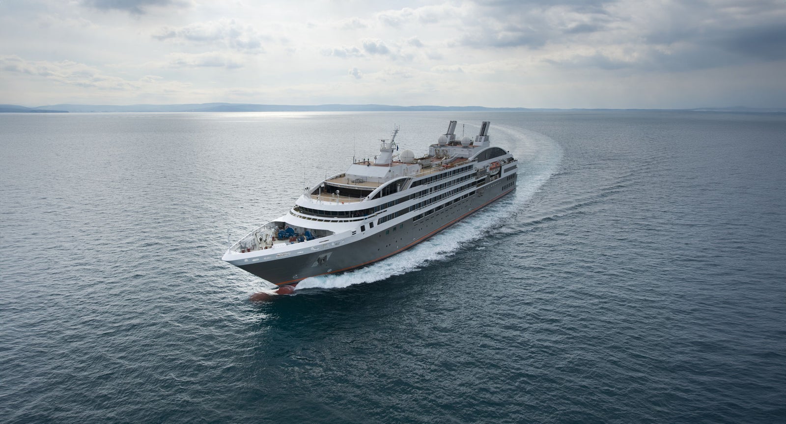 Fincantieri | Group - Business - Products - Cruise Ships - Le Boreal: Sleek modern cruise ship in operation navigating calm open waters under cloudy sky, multiple decks and visible chimneys, setting emphasizes premium travel experience, tranquility and adventure.