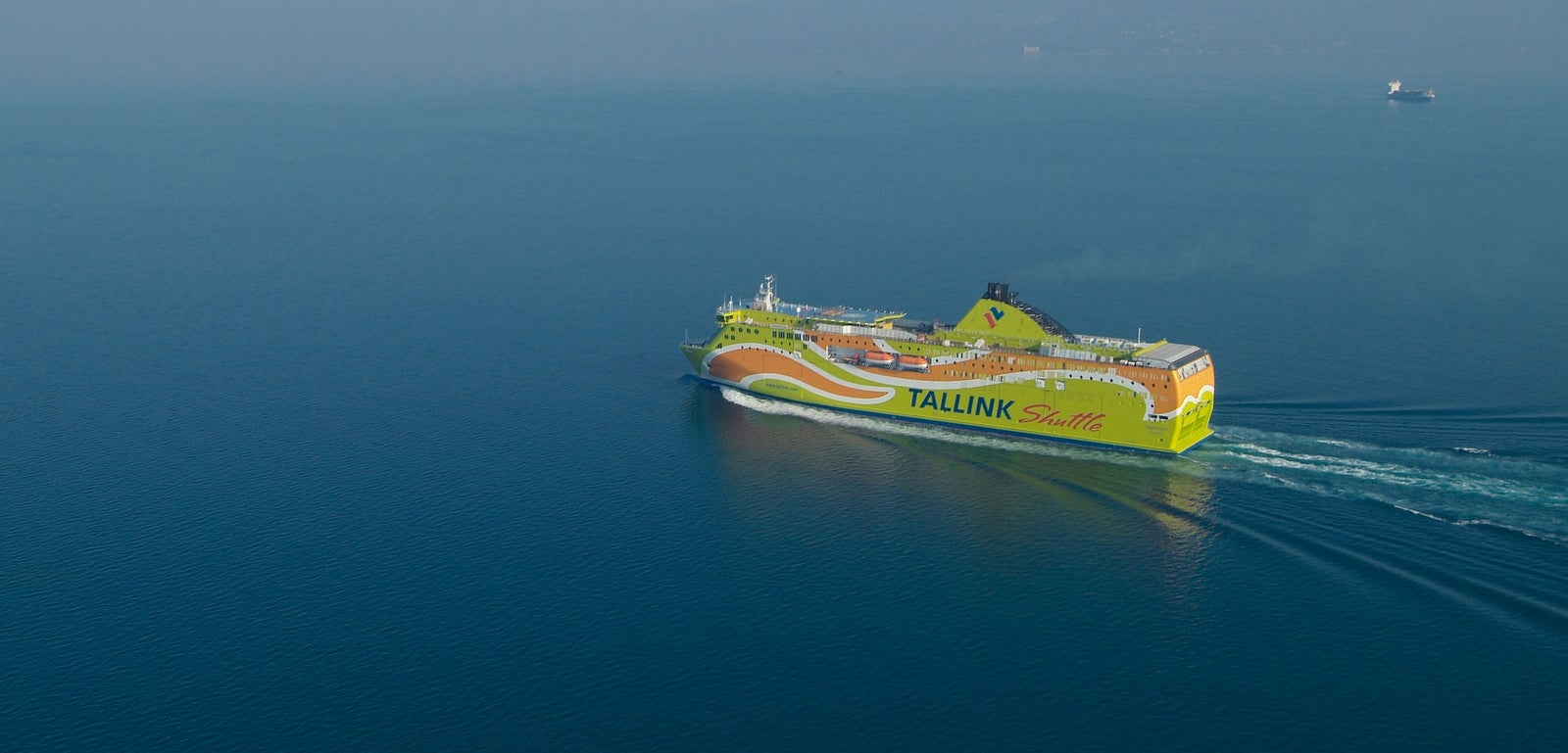 Fincantieri | Group - Business - Products - Ferries - Superstar: Tallink Shuttle ferry in operation, vibrant green and yellow color scheme, visible "Tallink" and "Shuttle" text, sailing through calm open waters, clear blue sky.