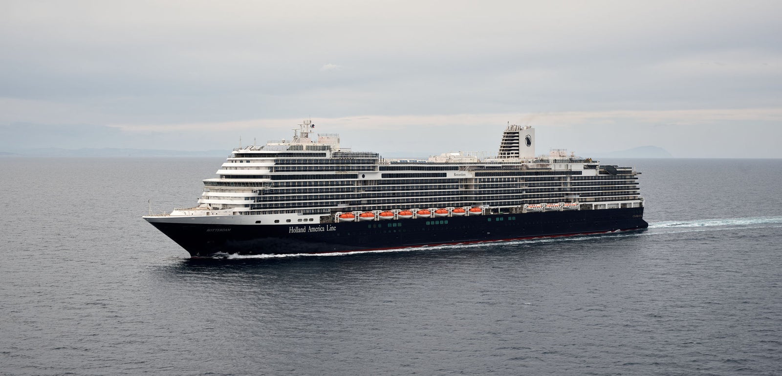 Fincantieri | Group - Business - Products - Cruise Ships - Rotterdam: Large Holland America Line operational cruise ship sailing on calm waters under cloudy sky, multiple decks and visible lifeboats along its sides.