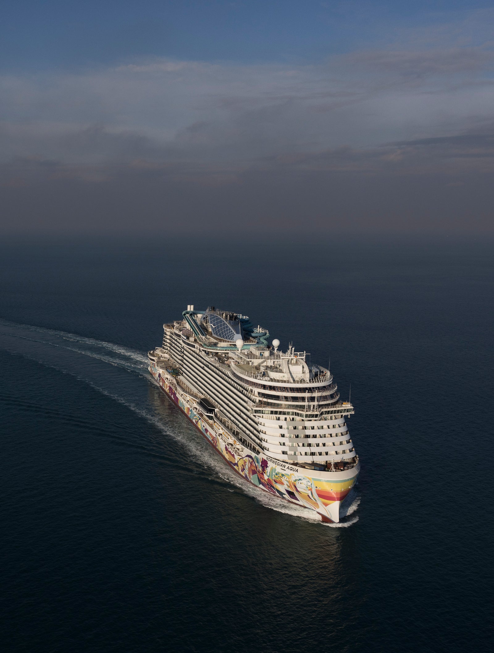  Fincantieri | Group - Business - Products - Cruise Ships - Norwegian Aqua: Aerial side view of Norwegian Aqua cruise ship in operation, sailing on calm sea, visible white wake trail.