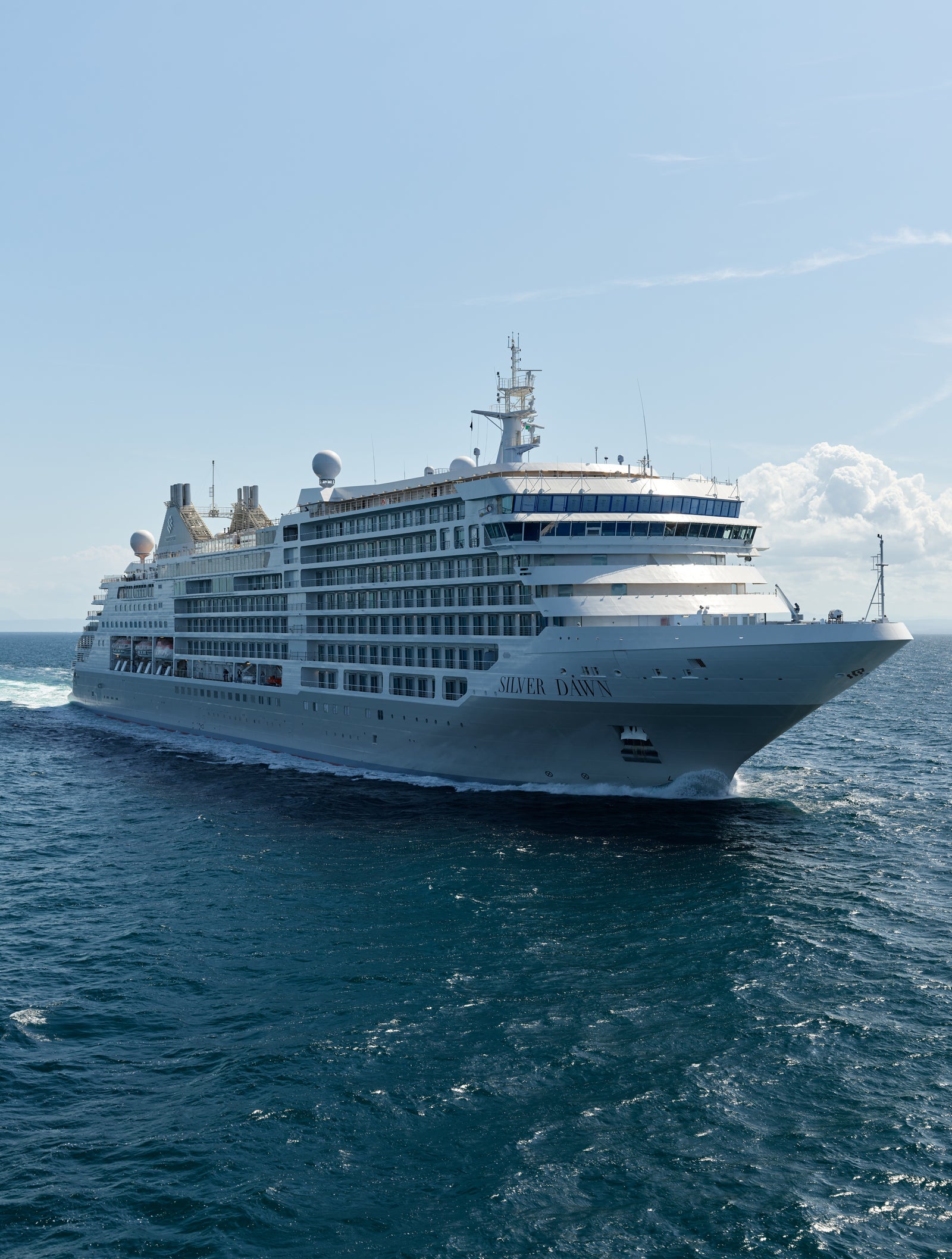 Fincantieri | Group - Business - Products - Cruise Ships - Silver Dawn: Large luxury cruise ship in operation gliding through open ocean under clear blue sky, multiple decks and modern design details, name 'Silver Dawn' clearly visible on hull, calm waters and bright daylight enhance serene majestic atmosphere.