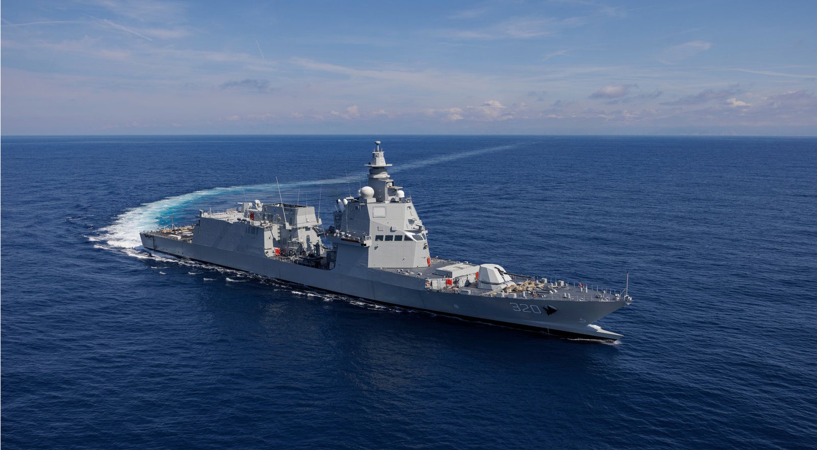 Fincantieri | Group - Companies - Subsidiaries and Affiliates - Orizzonte Sistemi Navali: Modern operational military ship sailing on deep blue ocean under a clear sky, equipped with advanced radars and armaments, distinctive wake emphasizing speed and agility; contrast between calm environment and the powerful presence of the ship.