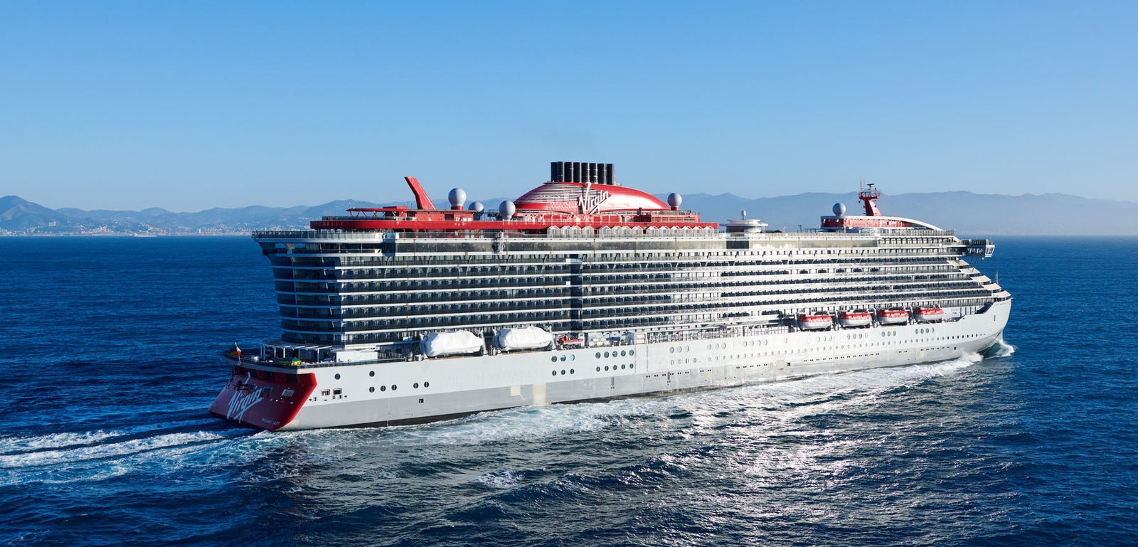 Fincantieri | Group - Business - Products - Cruise Ships - Brilliant Lady: Large operational cruise ship with modern design and distinctive red accents, multiple decks, name 'Brilliant Lady' visible on hull, sailing in calm waters under partly cloudy sky, maritime context.