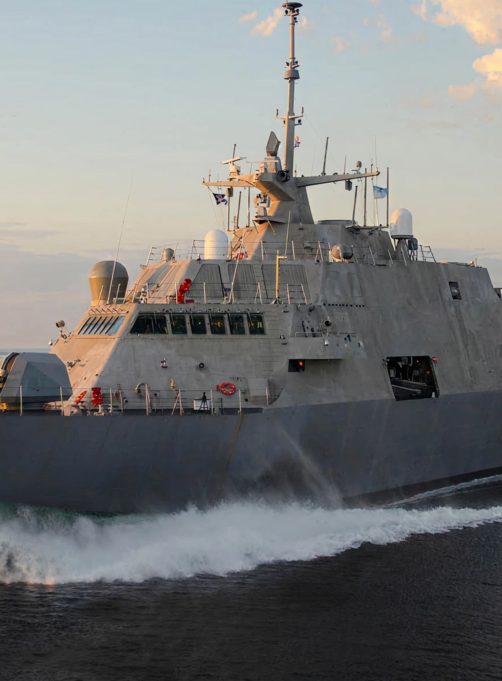 Fincantieri | Gruppo - Società - Controllate e collegate - Marine Systems North America: Grande nave militare operativa in navigazione su acque aperte al tramonto, design moderno e filante, antenne ed equipaggiamenti visibili sul ponte; numero ‘3’ ben visibile sullo scafo, onde calme e cielo soft con nuvole sparse che valorizzano la scena.
