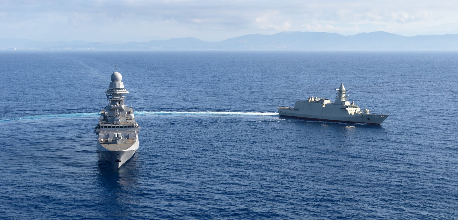 Fincantieri | Group - Business - Products - Defence Vessels - Corvettes - Abu Dhabi class: Close-up view of naval radar system mounted on warship, angular components and antennas visible, maritime environment and clear sky, advanced technology.