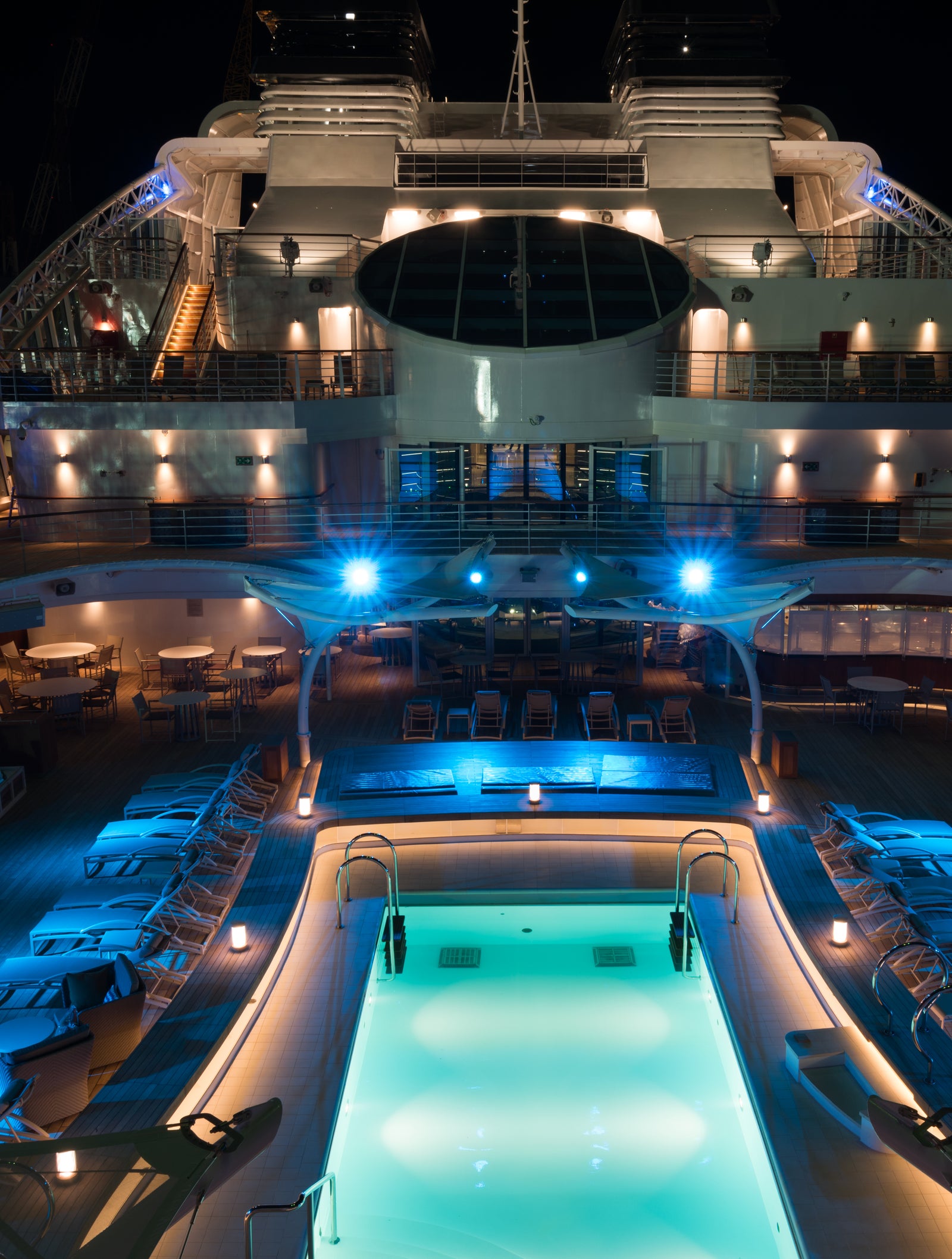 Fincantieri | Gruppo - Business - Prodotti - Navi da Crociera - Seabourn Encore: Vista notturna del ponte piscina della Seabourn Encore, piscina centrale, lettini lounge e illuminazione d’atmosfera blu.