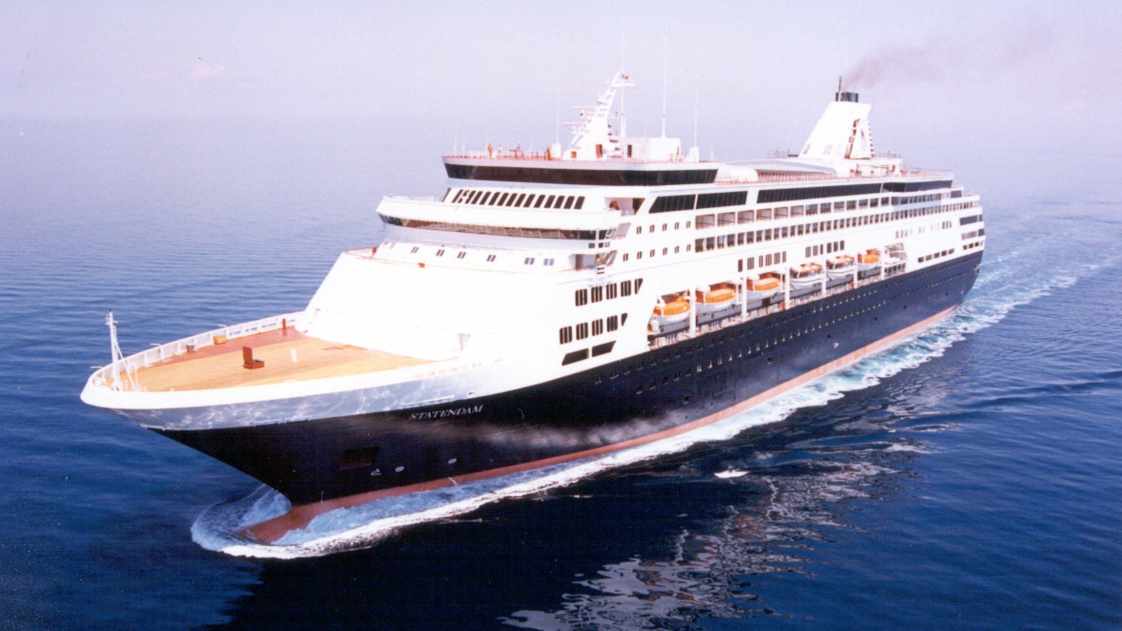 Fincantieri | Group - Business - Products - Cruise Ships - Statendam: Side view of Statendam cruise ship in operation navigating, multiple decks, visible lifeboats, sleek design, smoke from funnel.