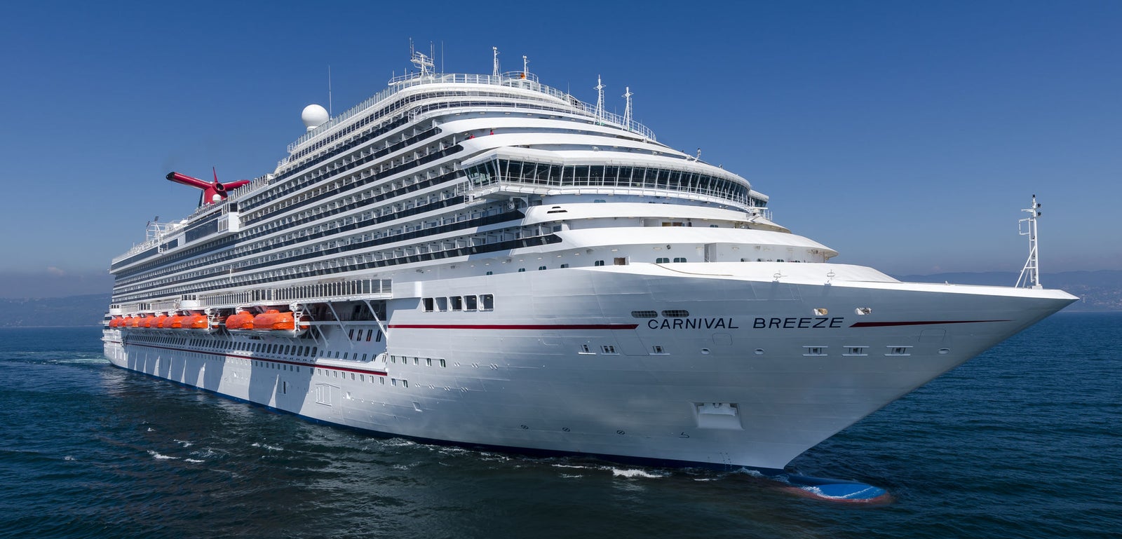 Fincantieri | Group - Business - Products - Cruise Ships - Carnival Breeze: White operational cruise ship with multiple decks navigating calm open waters under clear blue sky, Carnival Breeze name visible on hull, funnel with recognizable Carnival logo, scene highlights grandeur of ship and serene marine environment.