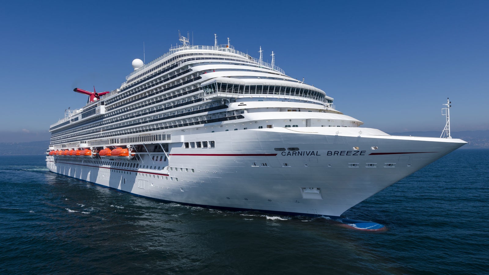 Fincantieri | Group - Business - Products - Cruise Ships - Carnival Breeze: White operational cruise ship with multiple decks navigating calm open waters under clear blue sky, Carnival Breeze name visible on hull, funnel with recognizable Carnival logo, scene highlights grandeur of ship and serene marine environment.