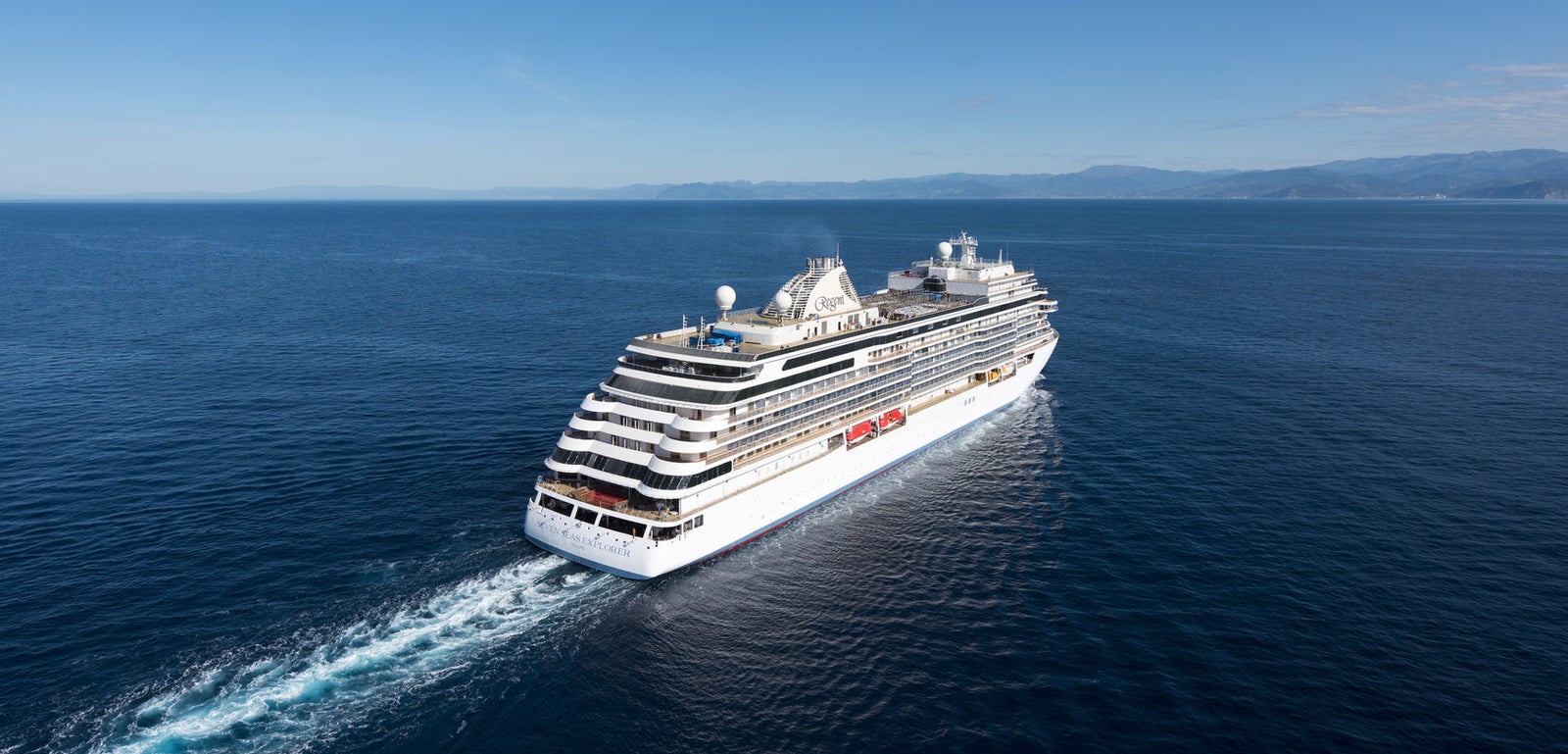 Fincantieri | Gruppo - Business - Prodotti - Navi da Crociera - Seven Seas Explorer: Grande nave da crociera moderna operativa con molteplici ponti e balconi visibili, naviga su acque calme sotto cielo limpido, esperienza di viaggio lussuosa e ampia vista marina in atmosfera serena.