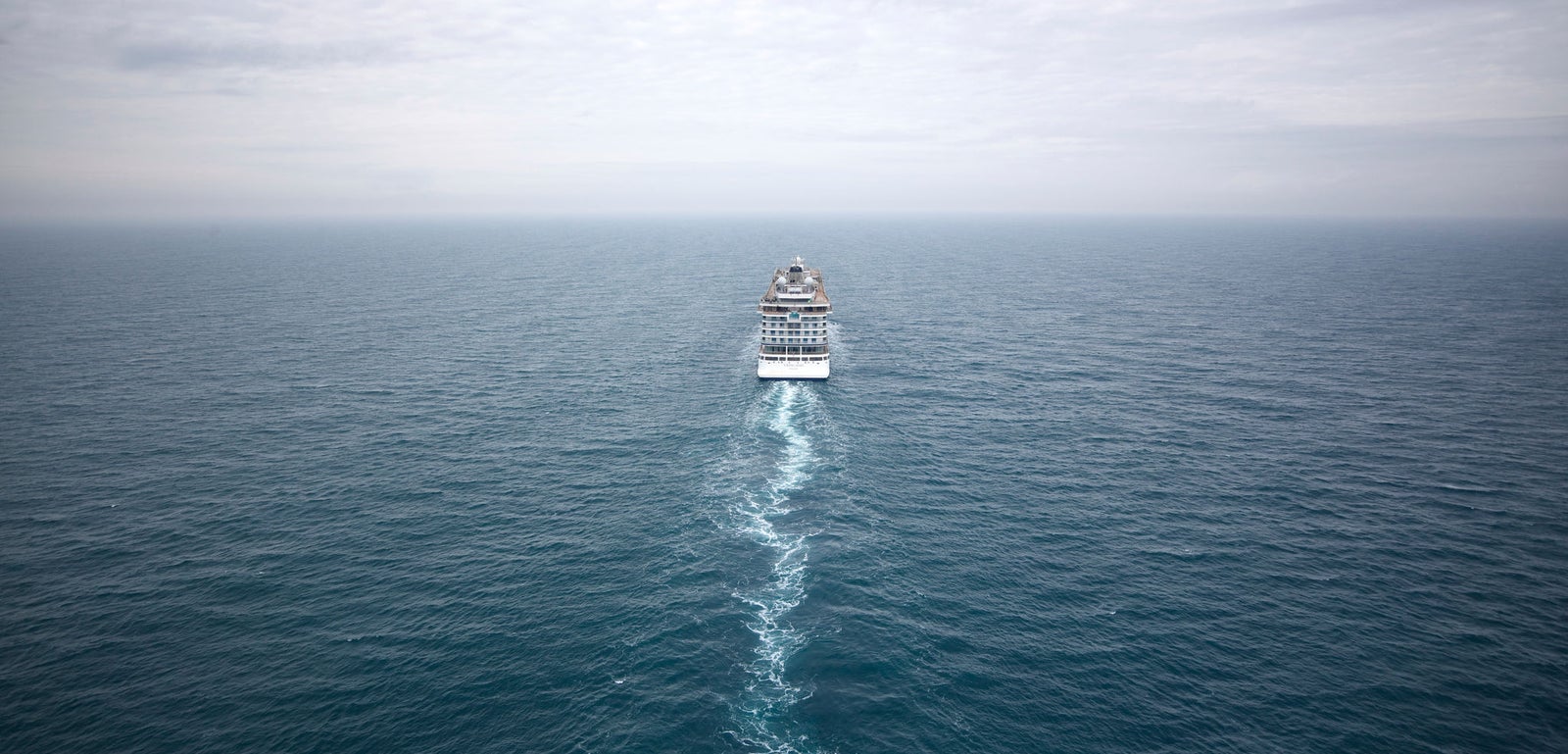 Fincantieri | Group - Business - Products - Cruise Ships - Viking Mars: Large cruise ship in operation, traveling through vast open ocean under cloudy sky, visible trail in water emphasizing movement, scene conveys adventure and tranquility in expansive blue sea.
