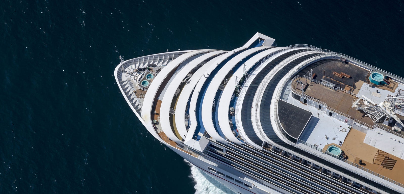 Fincantieri | Group - Business - Products - Cruise Ships - Carnival Breeze: Aerial view of large luxury cruise ship in operation sailing on deep blue waters, multiple decks, pools and recreation areas, curvaceous architecture and white exterior stand out against dark sea, highlights ship’s grandeur and refined design.