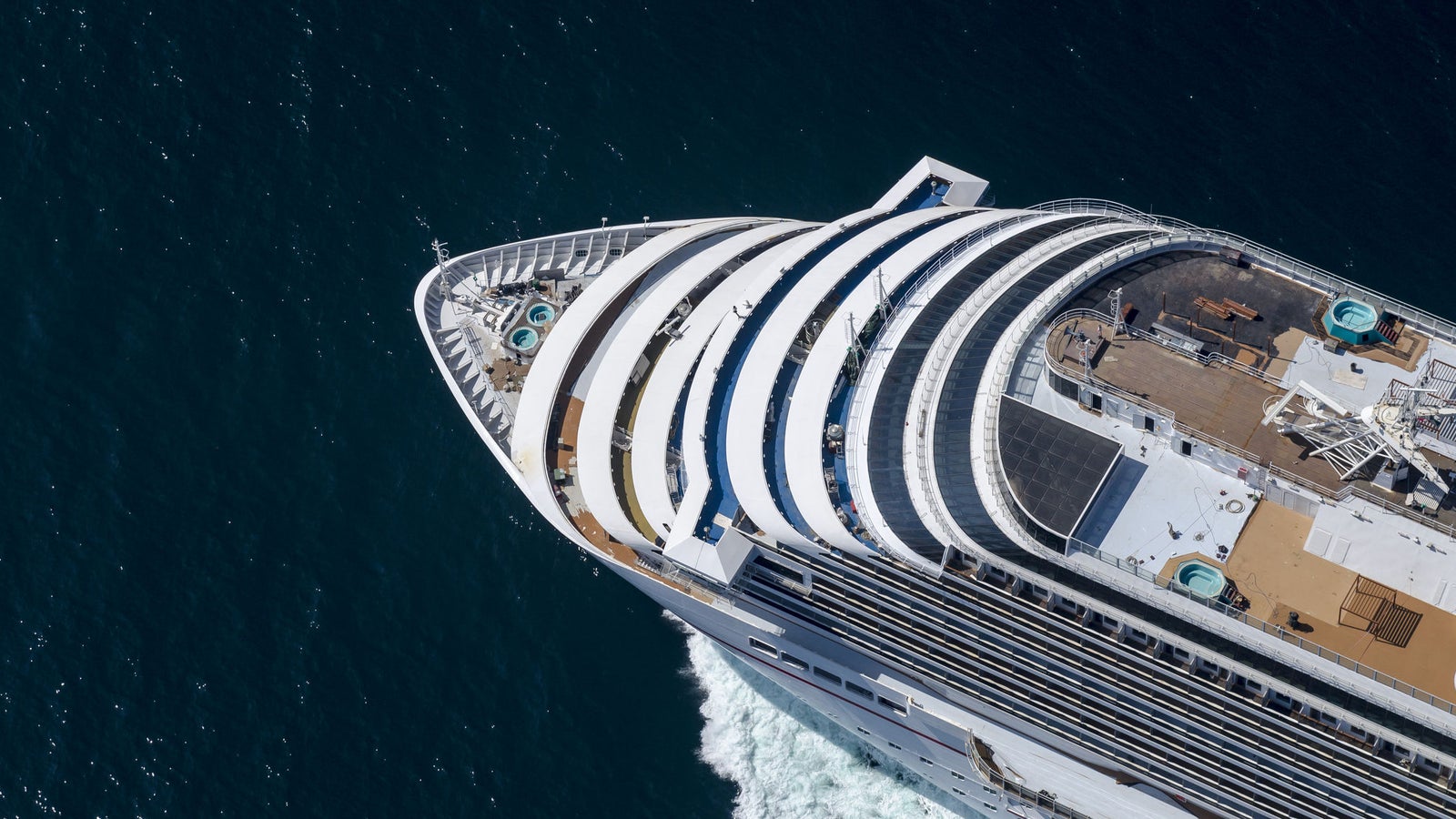 Fincantieri | Group - Business - Products - Cruise Ships - Carnival Breeze: Aerial view of large luxury cruise ship in operation sailing on deep blue waters, multiple decks, pools and recreation areas, curvaceous architecture and white exterior stand out against dark sea, highlights ship’s grandeur and refined design.