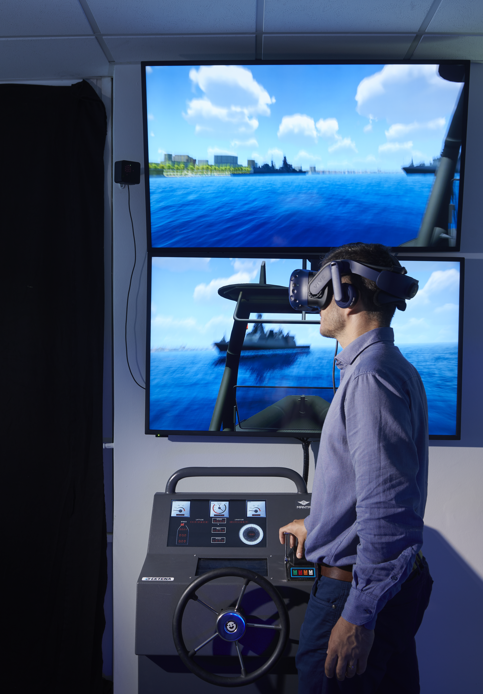 Fincantieri | About Us - Global Presence: Man wearing a virtual reality headset interacts with a nautical simulator, two screens with maritime views and a control panel with steering wheel, indoor environment focused on immersive technology.