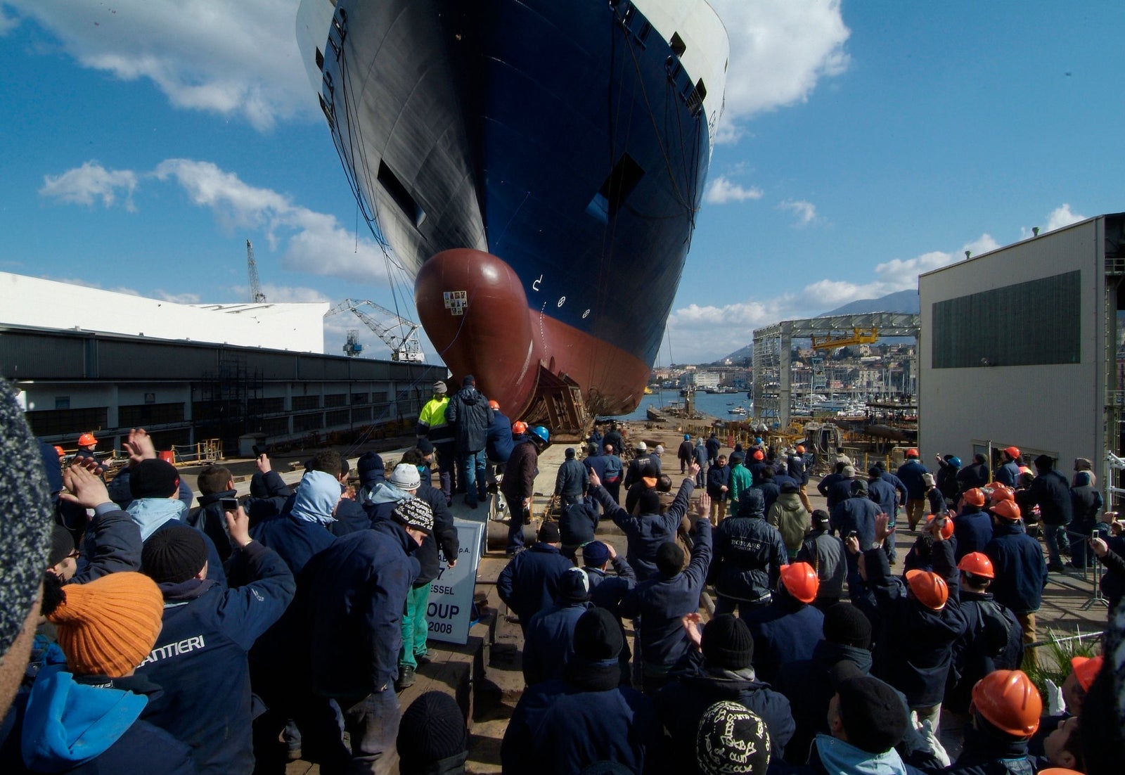 Prodotto - Traghetto Barcellona Grimaldi Lines: Vista frontale della nave in bacino di carenaggio, scafo imponente e design metallico, impalcature e strutture industriali, scritta FINCANTIERI visibile sulle impalcature.