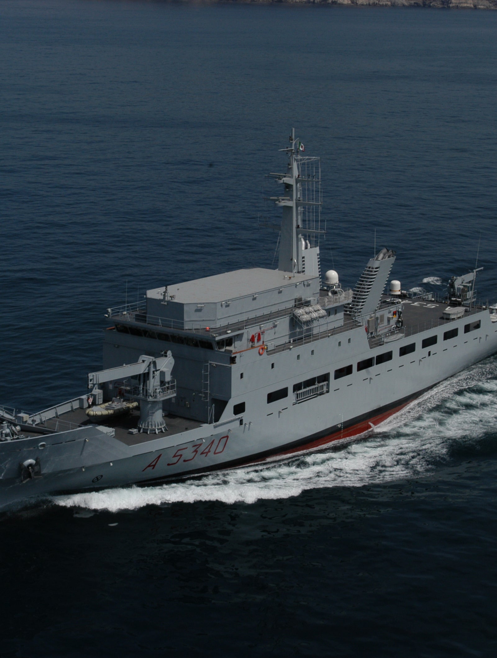 Fincantieri | Group - Business - Products - Specialised Units - Elettra ship: Side view of operational ship underway, gray hull, number A 5340 clearly visible, prominent wake, rocky coast in background.