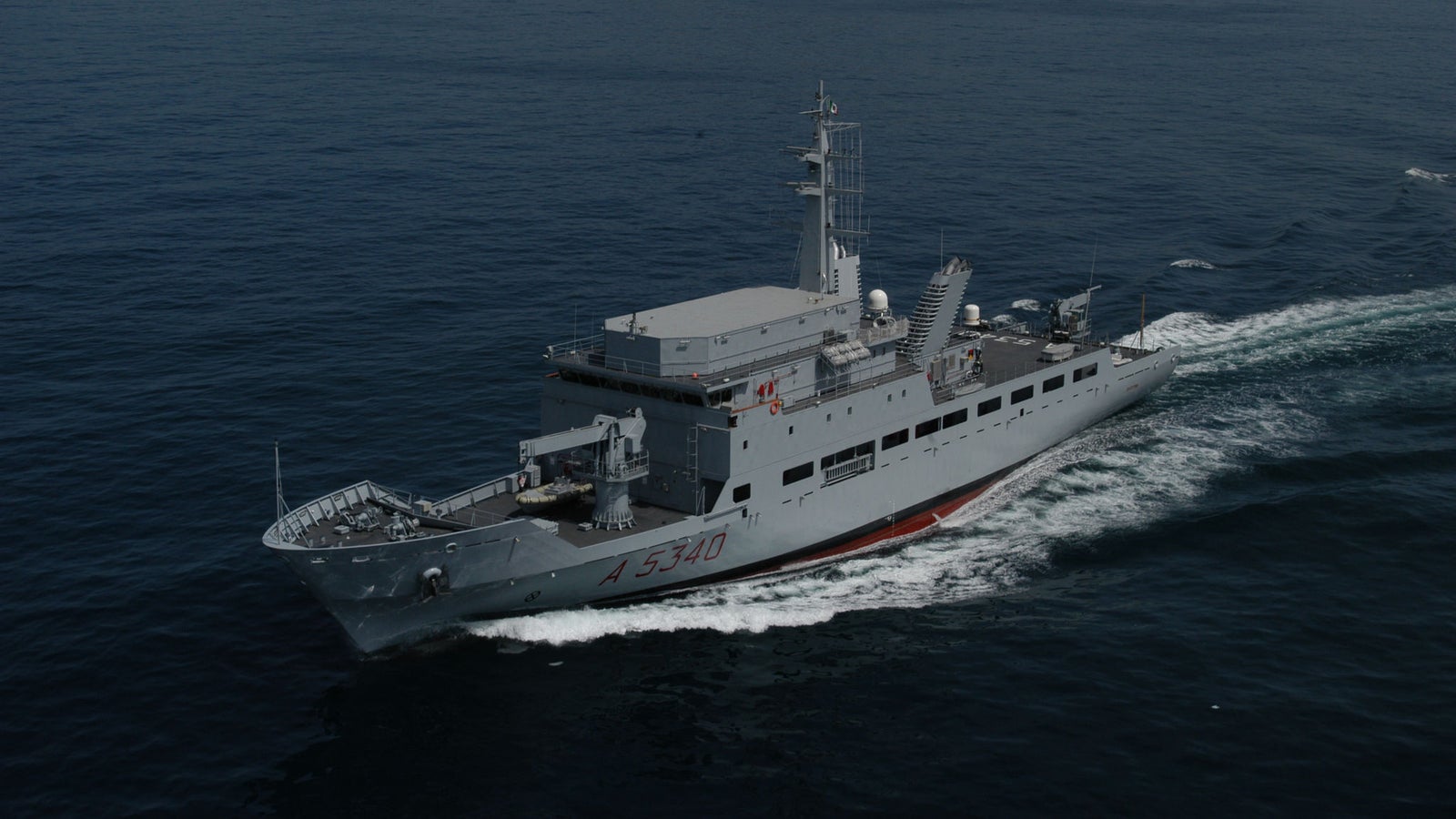 Fincantieri | Group - Business - Products - Specialised Units - Elettra ship: Side view of operational ship underway, gray hull, number A 5340 clearly visible, prominent wake, rocky coast in background.