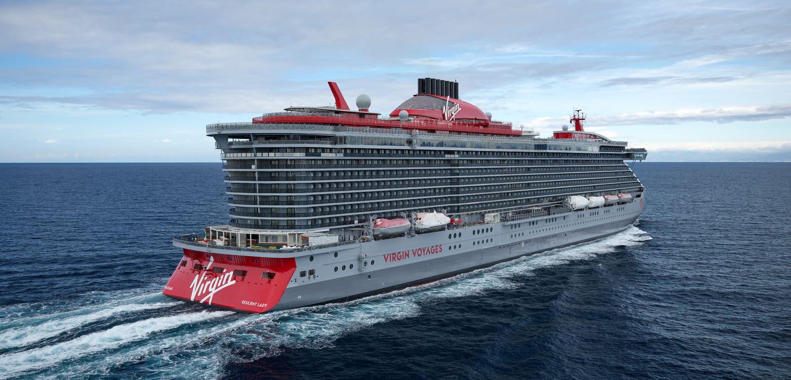 Fincantieri | Group - Business - Products - Cruise Ships - Resilient Lady: Large modern operational cruise ship with elegant design and red details, multiple decks, name 'Resilient Lady' clearly visible on hull, distinctive red funnel, sailing in calm waters under partly cloudy sky, atmosphere of luxury and maritime adventure.
