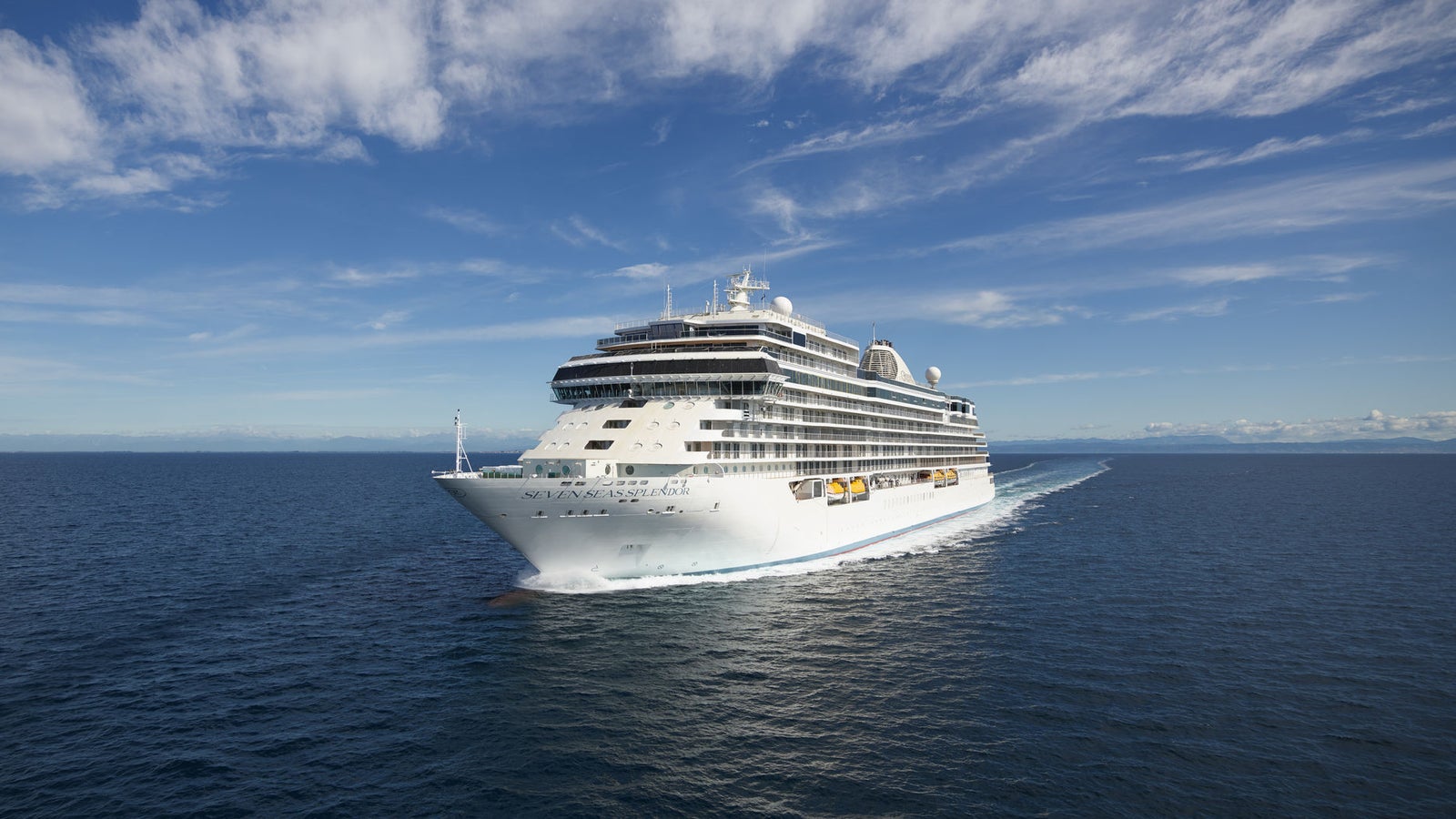 Fincantieri | Group - Business - Products - Cruise Ships - Seven Seas Splendor: Large modern operational white cruise ship with multiple decks and visible lifeboats, sailing on calm waters under clear sky, luxurious and tranquil travel experience with wide ocean views.
