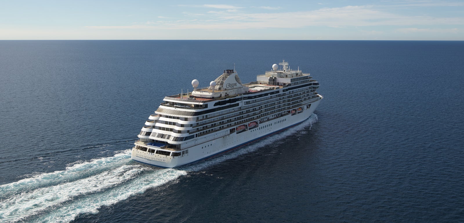 Fincantieri | Group - Business - Products - Cruise Ships - Seven Seas Splendor: Large modern luxury cruise ship in operation with multiple views of decks and balconies, sailing on calm waters with visible wake, clear blue sky and wide horizon, scene conveys tranquility and maritime adventure.