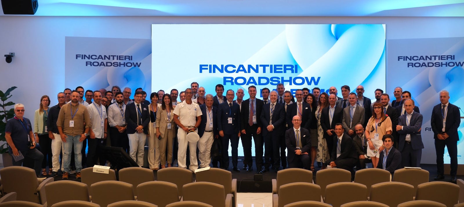 Fincantieri | Fornitori e Partner – Fincantieri Responsible Procurement: Foto di gruppo numeroso di partecipanti al Fincantieri Roadshow in sala conferenze moderna, schermo digitale con nome evento sullo sfondo, uomini e donne di varie età in abbigliamento business e casual, atmosfera professionale e collaborativa.