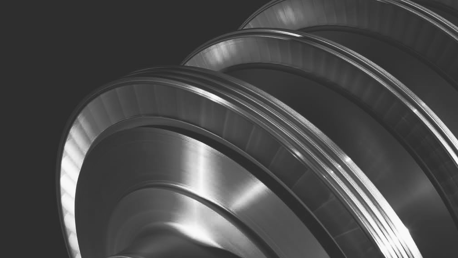 Fincantieri | Group - Business - Products - Equipment, Systems and Infrastructures - Steam turbines: Close-up of metallic turbine rotor with multiple fins, shiny surface and intricate detailing.