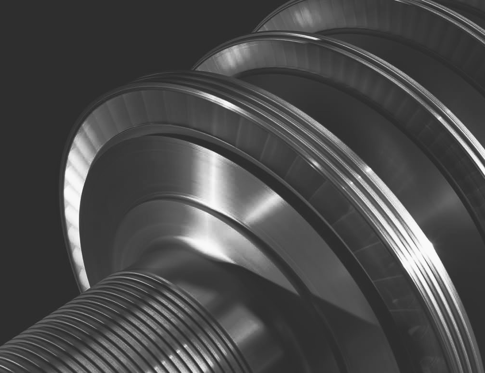  Fincantieri | Group - Business - Products - Equipment, Systems and Infrastructures - Steam turbines: Close-up grayscale image of machined metal component with concentric rings and threads; shaft with multiple precisely engineered stages or wheels.
