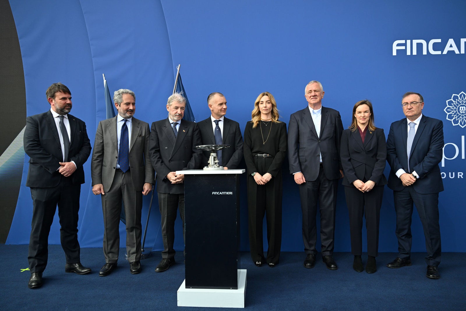  Newsroom - Press releases - 2026 - Fincantieri Group: Fincantieri:  Today triple ceremony for Fincantieri and Explora Journeys at Sestri Ponente: launche of Explora IV, coin ceremony for Explora V and steel cuttingfor Explora VI: Fincantieri and Explora Journeys management in formal attire pose in front of blue backdrop with ceremony podium.