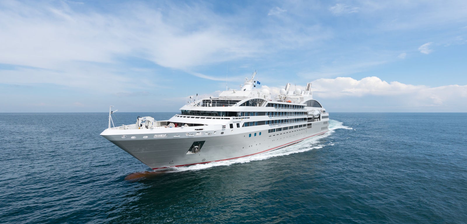 Fincantieri | Group - Business - Products - Cruise Ships - Le Soléal: Modern white cruise ship in operation gliding across calm blue waters under partly cloudy sky, multiple decks and sleek design suggest premium travel experience, serene ocean setting highlights ship’s grandeur and journey.