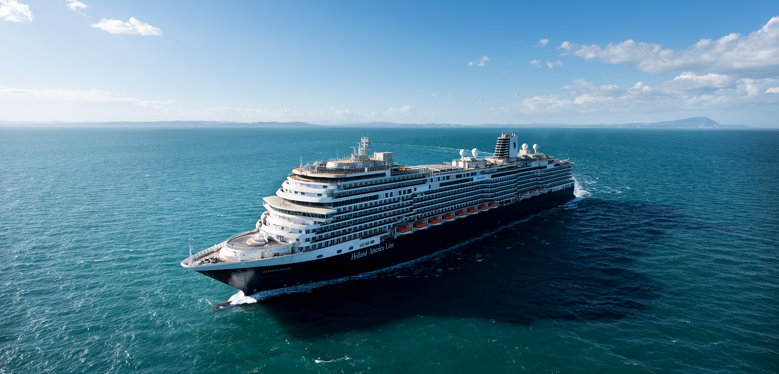  Fincantieri | Gruppo - Business - Prodotti - Navi da Crociera - Koningsdam: Grande nave da crociera di lusso operativa che naviga su acque calme e aperte sotto cielo azzurro luminoso, più ponti e design moderno, terra distante visibile all’orizzonte.