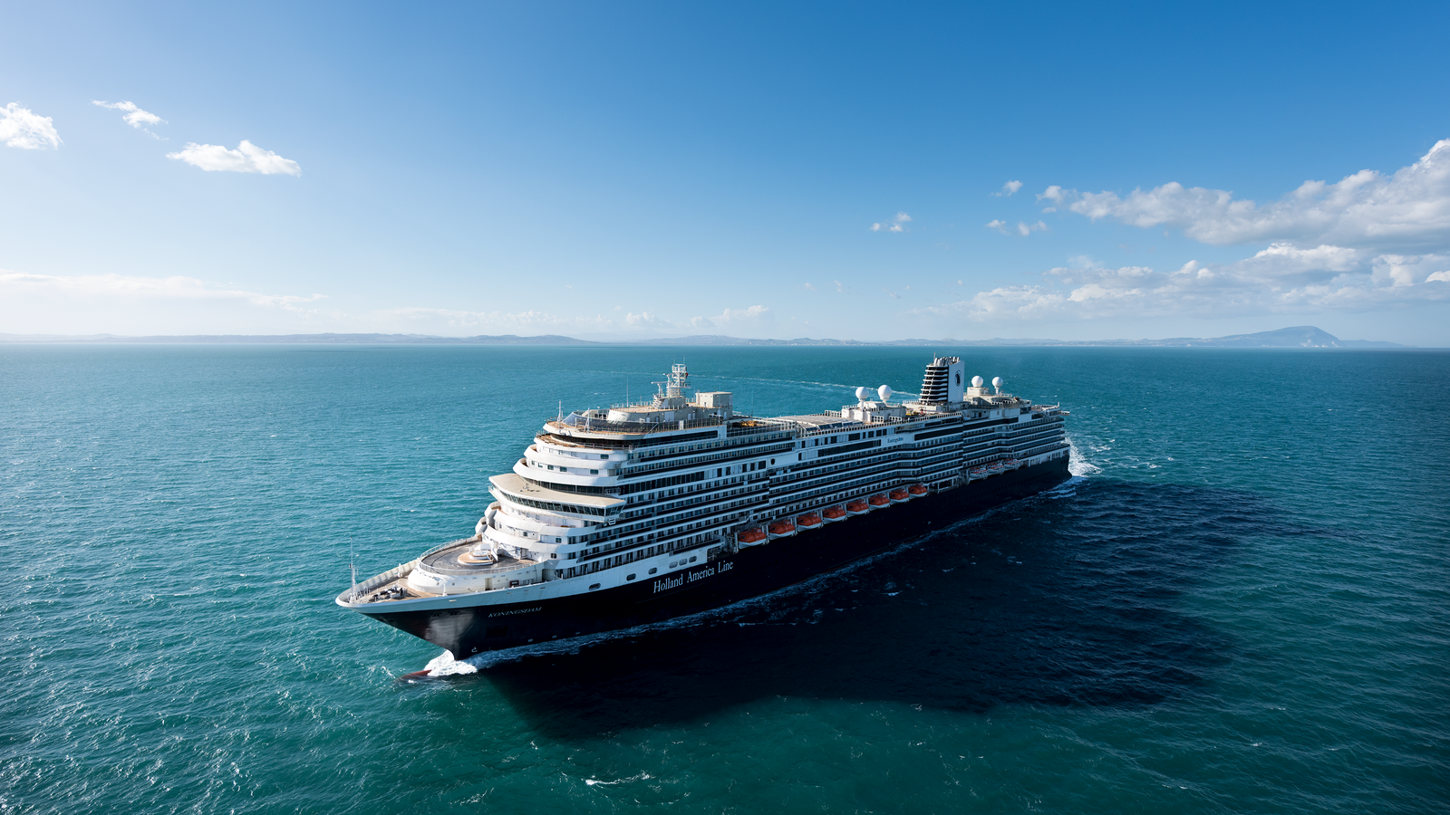  Fincantieri | Gruppo - Business - Prodotti - Navi da Crociera - Koningsdam: Grande nave da crociera di lusso operativa che naviga su acque calme e aperte sotto cielo azzurro luminoso, più ponti e design moderno, terra distante visibile all’orizzonte.