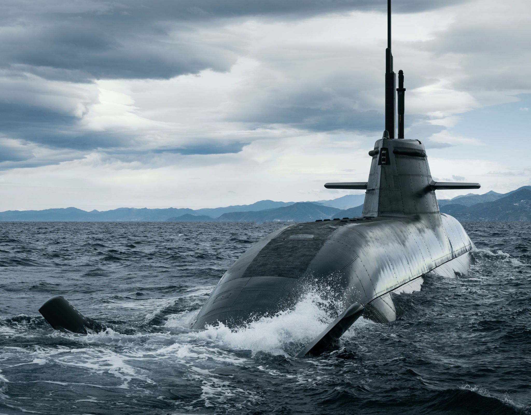 Fincantieri | Group - Sustainability - Industrial Excellence - Products: Modern operational military submarine surfacing from the sea amid choppy waves, cloudy sky and distant mountains on the horizon, dark design emphasizing power and stealth.