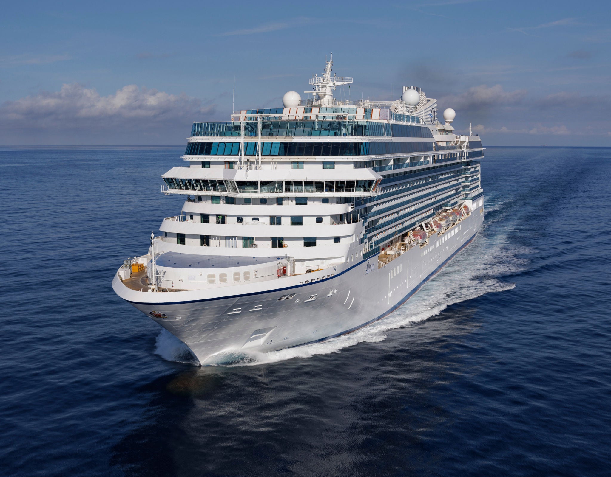 Fincantieri | Group - Sustainability - Industrial Excellence - Products: Modern operational cruise ship sailing on calm waters under a clear blue sky, multiple decks, large windows and outdoor areas for passengers, emphasis on size and leisure character.