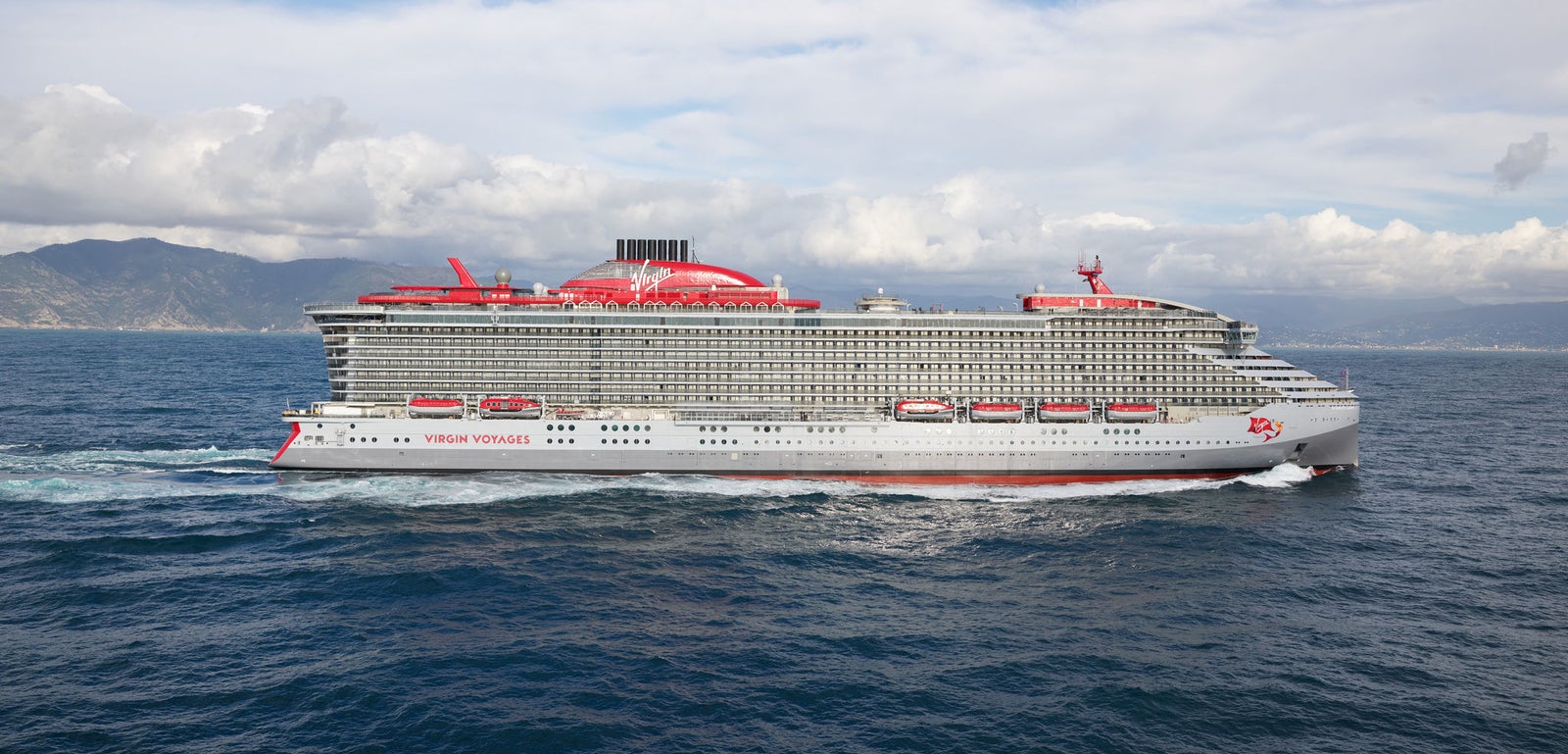 Fincantieri | Group - Business - Products - Cruise Ships - Scarlet Lady: Modern operational cruise ship with multiple decks and distinctive red funnel, 'Virgin' logo and 'Scarlet Lady' name clearly visible on hull, sailing on open waters under partly cloudy sky, serene sea and wide horizon view.