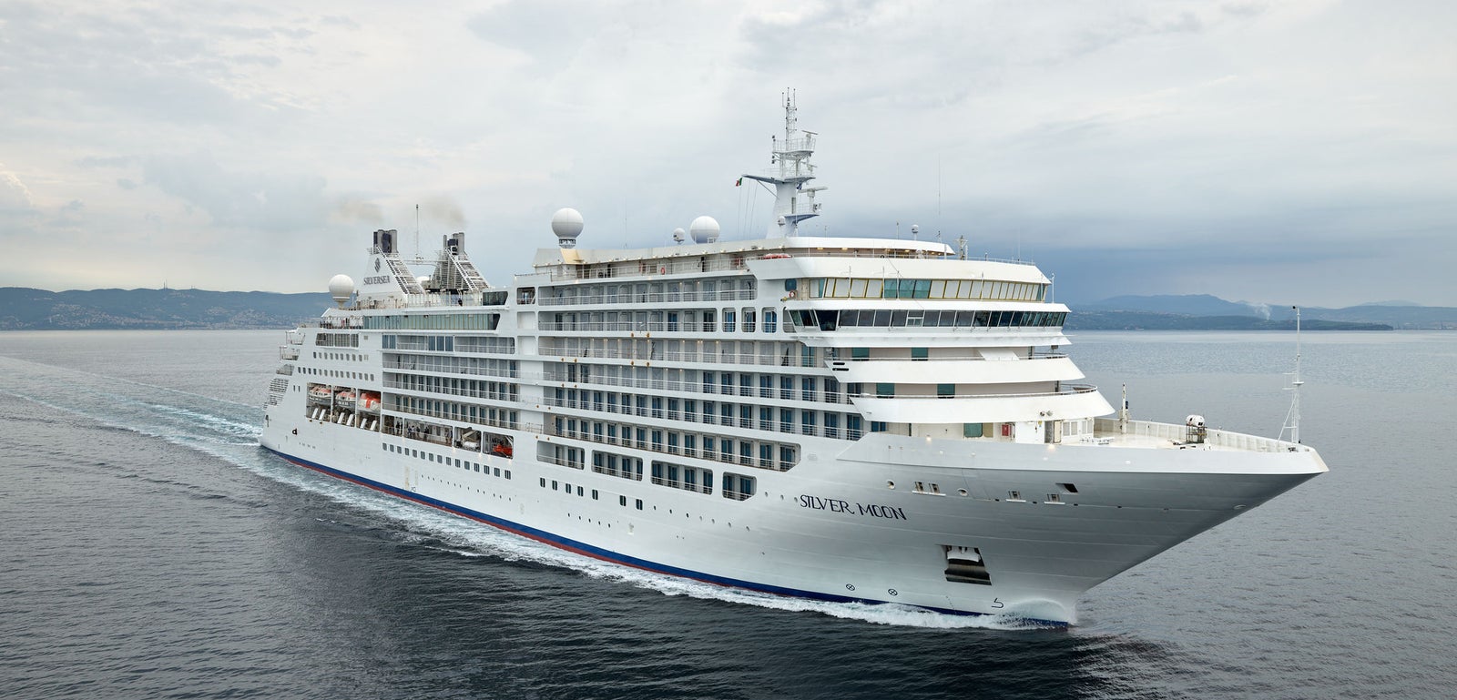 Fincantieri | Gruppo - Business - Prodotti - Navi da Crociera - Silver Moon: Vista laterale della nave Silver Moon operativa in navigazione, scafo bianco con ponti passeggeri su più livelli, scialuppe visibili e nome Silver Moon sull’imbarcazione.