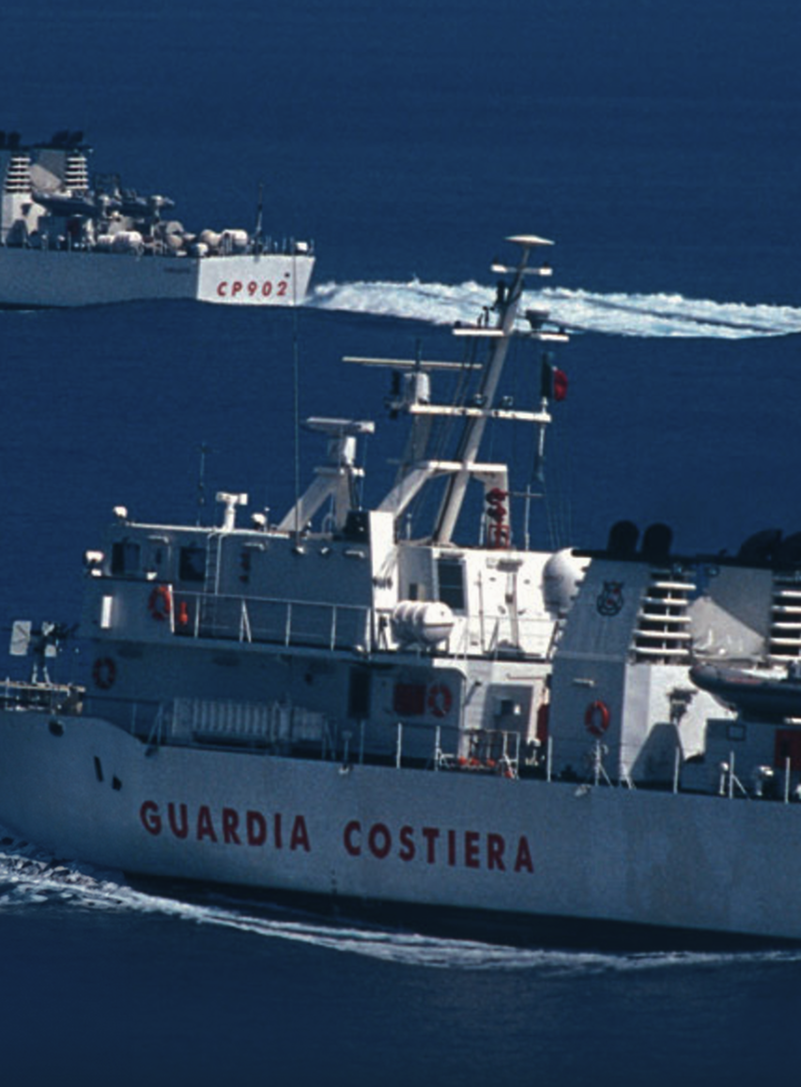 Fincantieri | Group - Subsidiaries and Affiliates - Isotta Fraschini Motori: Two Guardia Costiera ships seen navigating through calm blue waters, 'Guardia Costiera' and 'CP903' clearly visible on hulls; scene highlights maritime activity, ships equipped with antennas and naval equipment for coastal patrol operations.