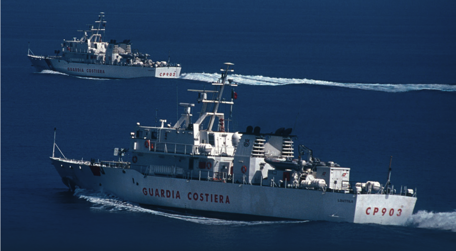 Fincantieri | Group - Subsidiaries and Affiliates - Isotta Fraschini Motori: Two Guardia Costiera ships seen navigating through calm blue waters, 'Guardia Costiera' and 'CP903' clearly visible on hulls; scene highlights maritime activity, ships equipped with antennas and naval equipment for coastal patrol operations.