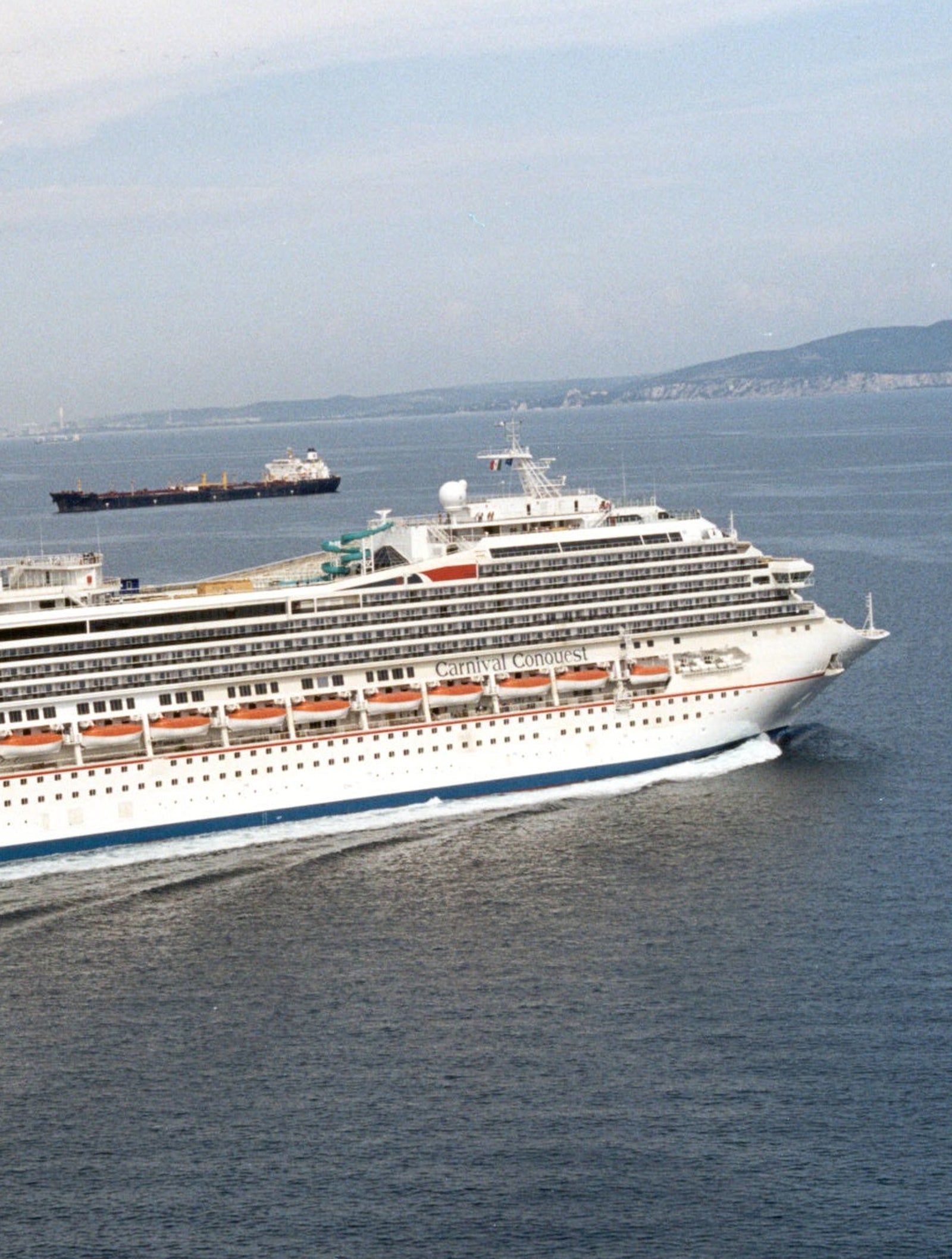 Fincantieri | Group - Business - Products - Cruise Ships - Carnival Triumph: Large operational cruise ship sailing on calm open waters, multiple decks including upper recreational areas, distinctive red and blue funnel clearly visible, white exterior and rows of windows.