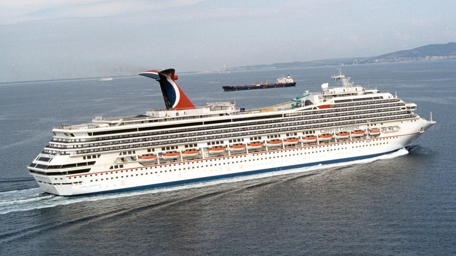 Fincantieri | Gruppo - Business - Prodotti - Navi da Crociera - Carnival Conquest: Vista laterale della nave Carnival Conquest operativa in navigazione, scafo bianco con fumaiolo rosso e blu distintivo e scialuppe visibili.