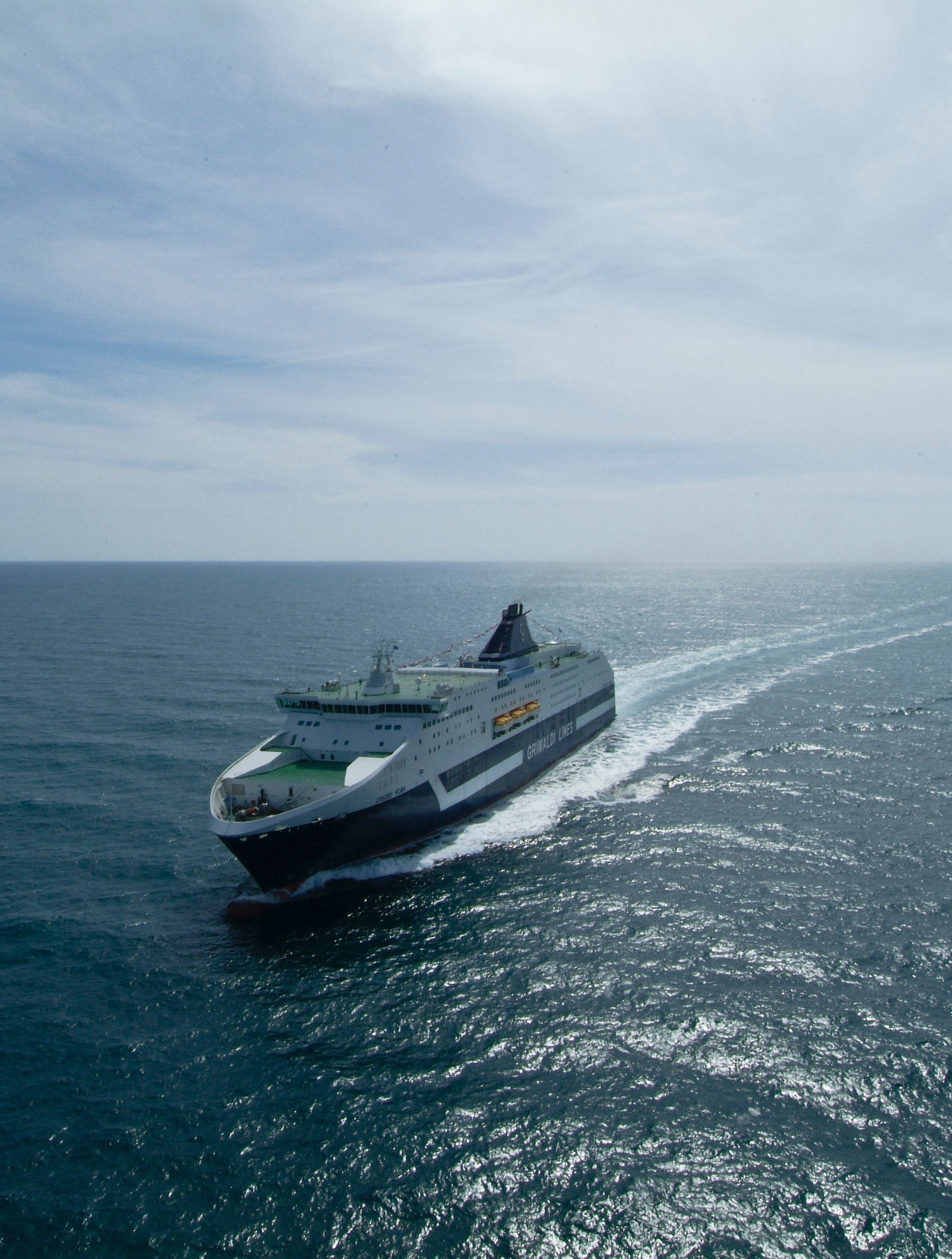 Fincantieri | Group - Business - Products - Ferries - Cruise Roma: Large "Grimaldi Lines" ferry in operation, cruising across open ocean, visible ship name on hull, wake behind vessel, partly cloudy sky.