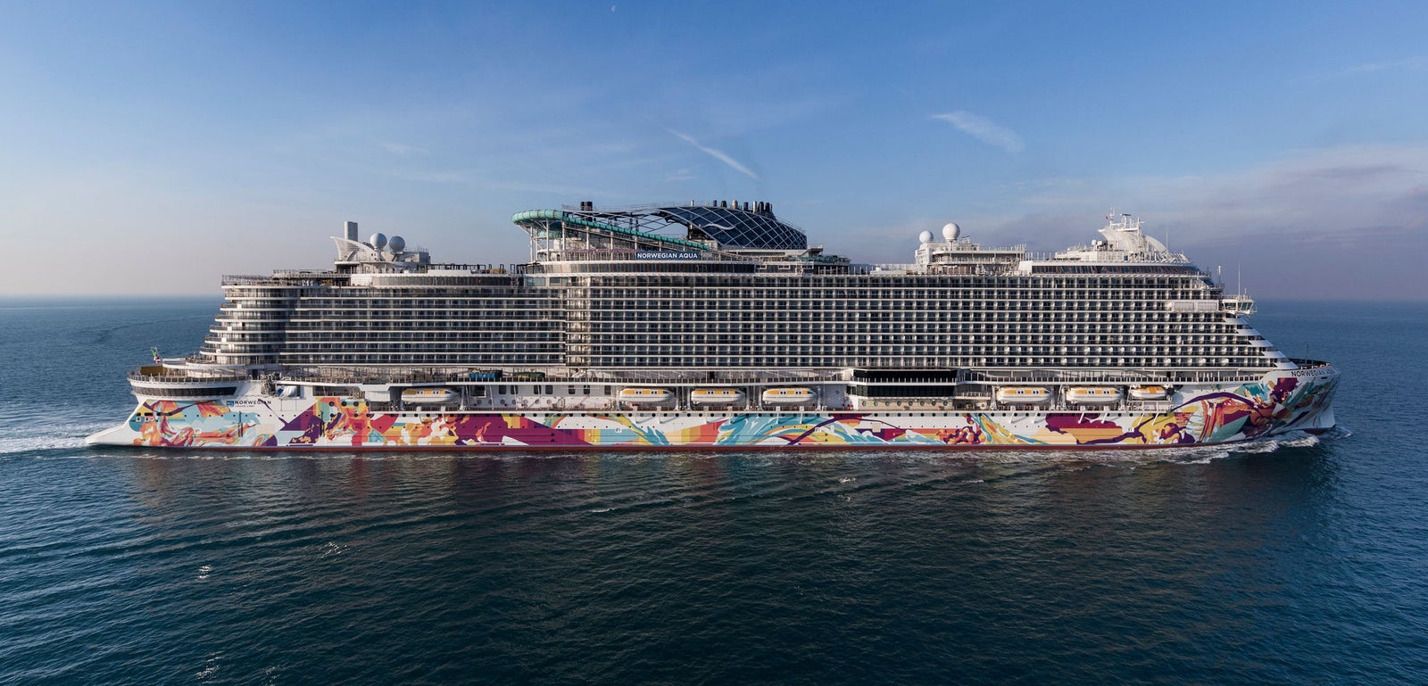 Fincantieri | Group - Business - Products - Cruise Ships - Norwegian Aqua: Full starboard side view of Norwegian Aqua cruise ship with colorful hull livery, blue sky and calm sea.