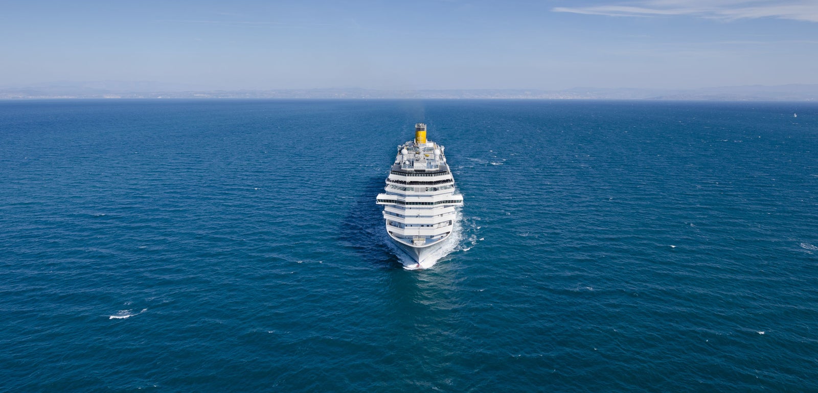 Fincantieri | Group - Business - Products - Cruise Ships - Costa Fascinosa: Massive cruise ship in operation navigating calm open waters under clear blue sky, centrally framed emphasizing grandeur and scale against vast ocean, serene setting highlights maritime travel tranquility.