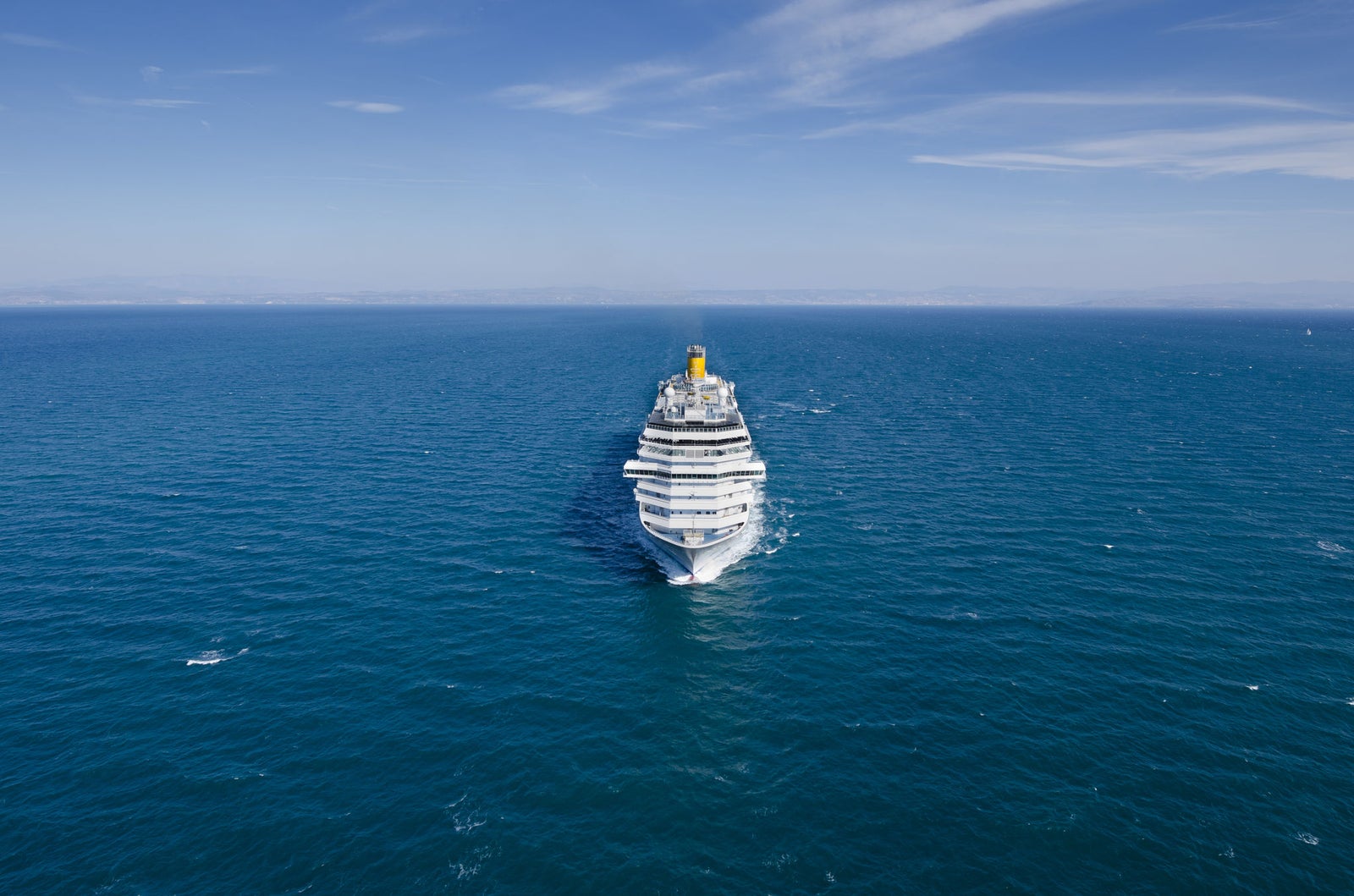 Fincantieri | Group - Business - Products - Cruise Ships - Costa Fascinosa: Massive cruise ship in operation navigating calm open waters under clear blue sky, centrally framed emphasizing grandeur and scale against vast ocean, serene setting highlights maritime travel tranquility.