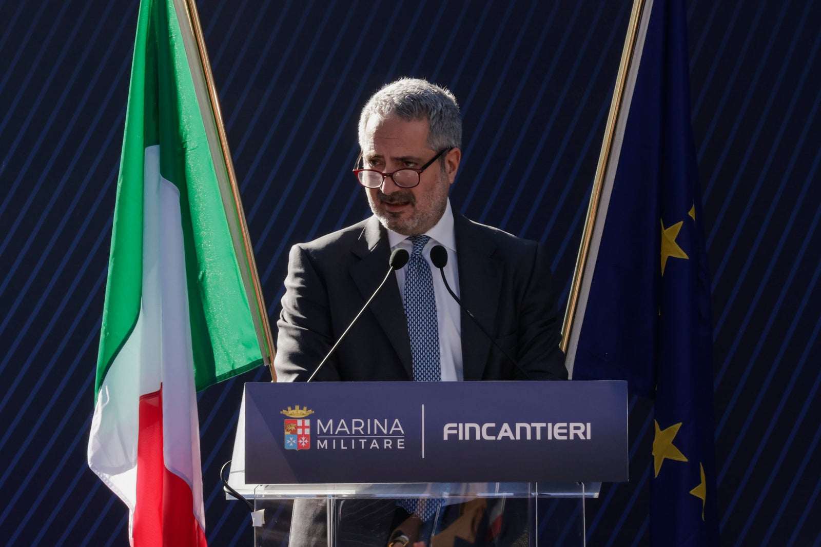 Newsroom - Press releases - 2026 - Fincantieri Group: Launch of the Italian Navy's "Quirinale" major hydro-oceanographic ship: fincantieri executive at podium with marina militare and european union flags speaks at launch ceremony.