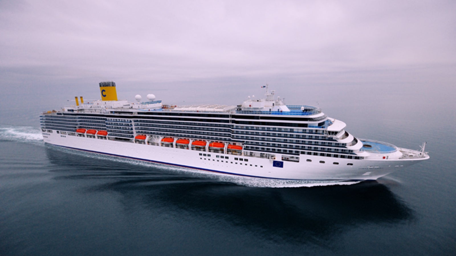 Fincantieri | Group - Business - Products - Cruise Ships - Costa Deliziosa: Side view of Costa Deliziosa cruise ship in operation, white hull with multi-level passenger decks, orange lifeboats and 'C' logo on funnel.