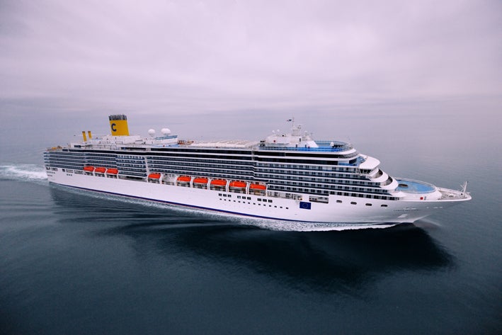 Fincantieri | Group - Business - Products - Cruise Ships - Costa Deliziosa: Large white cruise ship with multiple decks and orange lifeboats in operation sailing through calm open waters under overcast sky, visible 'C' logo on funnel, scene captures vessel grandeur and serene ocean setting.