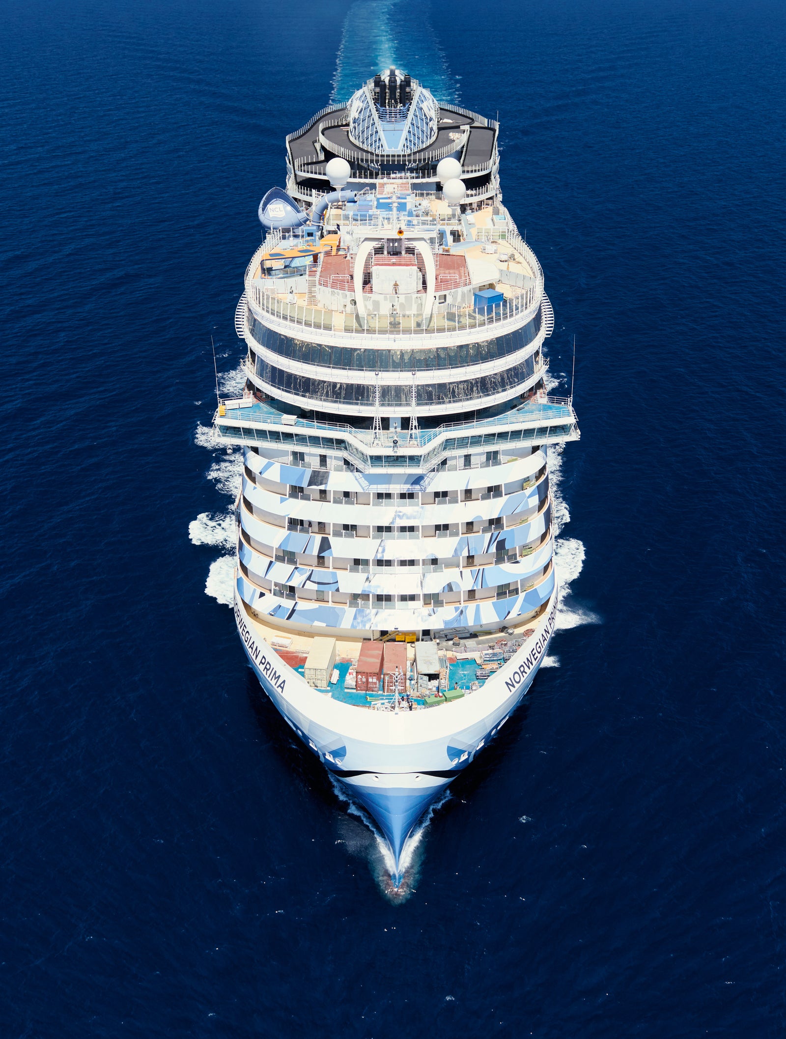 Fincantieri | Group - Business - Products - Cruise Ships - Norwegian Prima: Side view of Norwegian Prima cruise ship in operation, multiple decks with outdoor pool and observation areas, luxurious design.