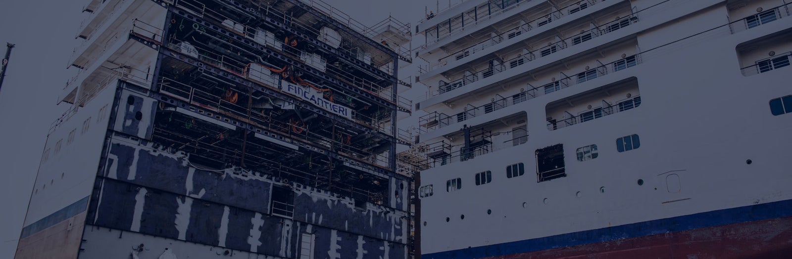 Fincantieri | Services - Ship Repair and Conversion: View of a partially constructed ship in the shipyard, presence of scaffolding and industrial equipment, visible structural details, highlighting the complexity and scale of the shipbuilding process.