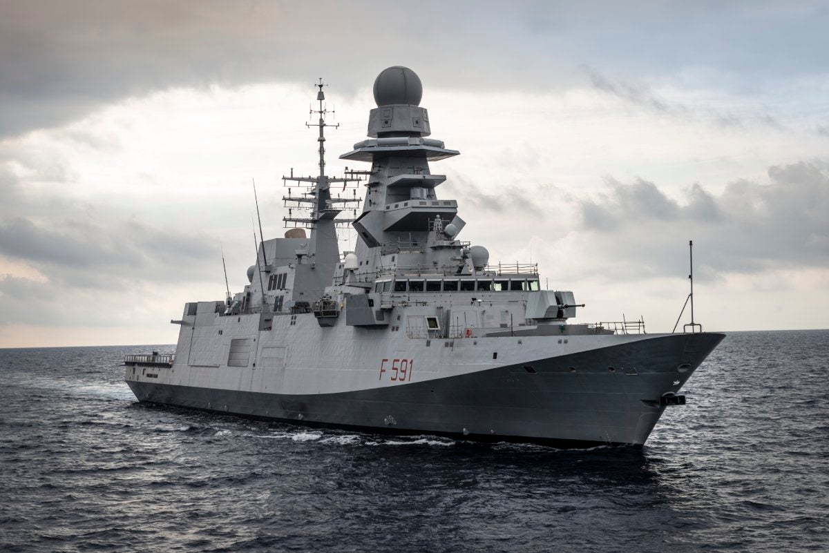 Fincantieri | Group - Companies - Subsidiaries and Affiliates - Fincantieri Arabia: Modern military frigate 'F591' operationally sailing on open sea under a cloudy sky, equipped with advanced radars and communication towers, ocean environment and dramatic atmosphere.